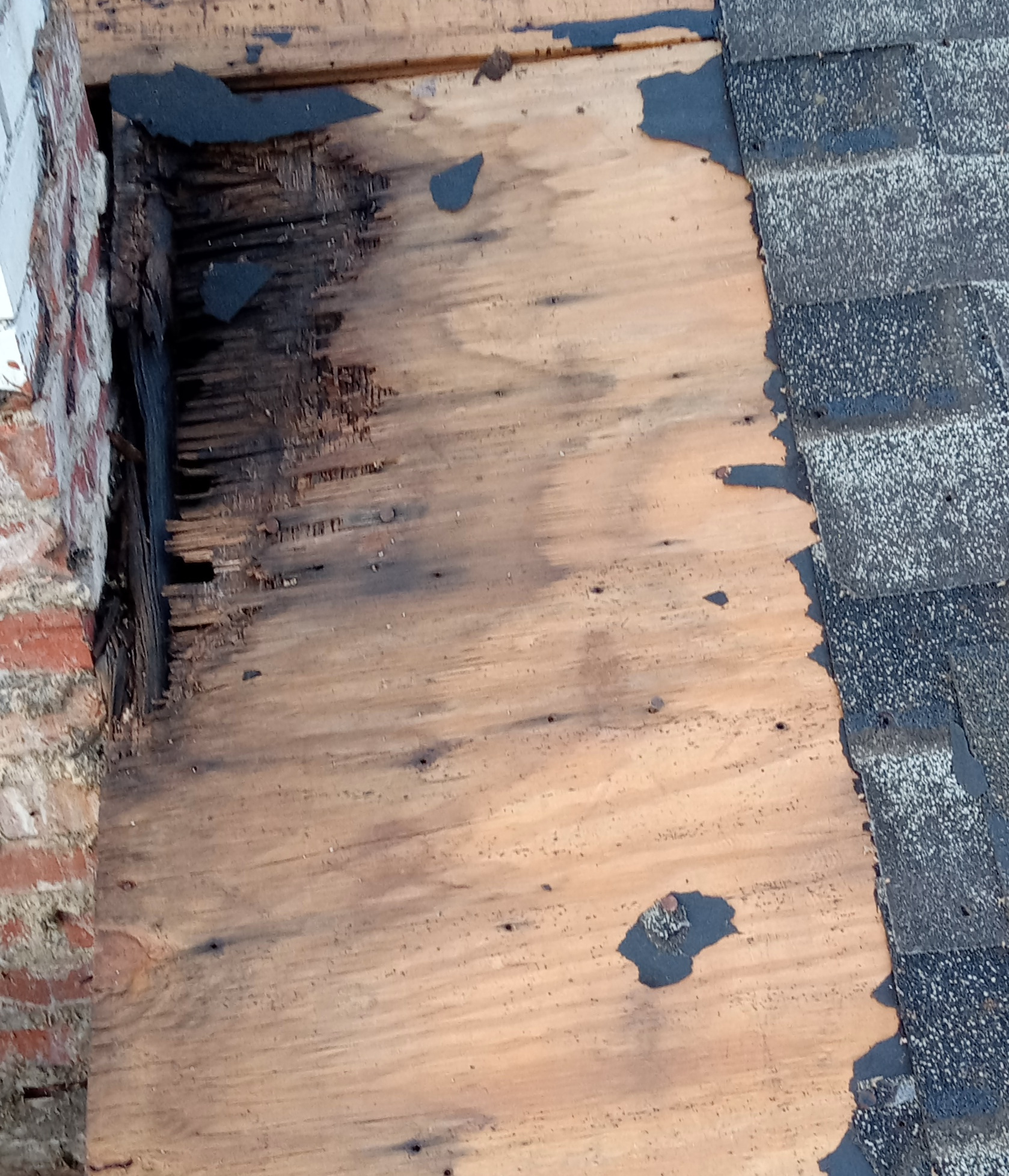 Water-deteriorated roof decking exposed beside a chimney